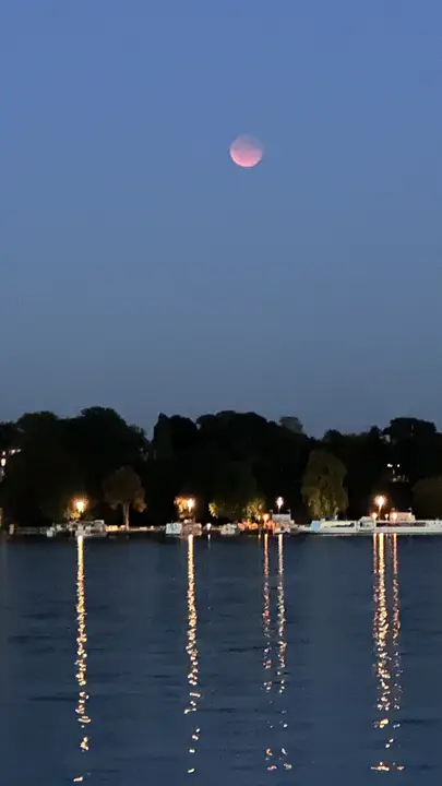 Roter Mond über dem nächtlichen Wannsee mit Lichterspiegelungen